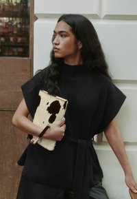 Černý pletený top s vysokým límcem a volnými rukávy, doplněný kabelkou s kravským potiskem a koženým popruhem.