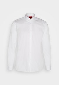 Chemise blanche à manches longues avec col classique et boutonnage sur le devant, avec une étiquette intérieure rouge au col.
