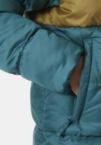 Tyrkysová péřová bunda s lesklým povrchem, s žlutou kapucí, žebrovanými manžetami a zipovou kapsou na levé straně.