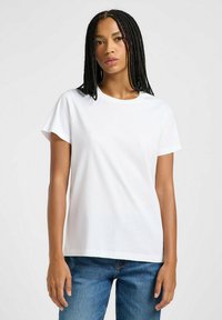 T-shirt bianco in cotone con maniche corte, scollatura rotonda, vestibilità ampia e texture liscia, abbinato a jeans in denim blu.
