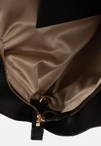 Interno di una borsa a tracolla in pelle nera con texture, rivestimento in raso beige, zip dorata e un attacco per portachiavi.