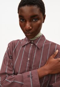 Maroon striped shirt with a button-down collar, white and blue stripes, and embroidered detail on the cuff. Smooth fabric texture.