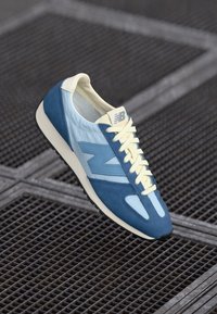 Blue and light blue suede and mesh sneaker with yellow laces and branding. Classic design with a textured sole and sleek silhouette.