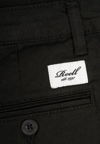 Černé kalhoty s bílou štítkem s nápisem „Reell est. 1997“, knoflíkem a malou kapsou s jemnými šicími detaily.