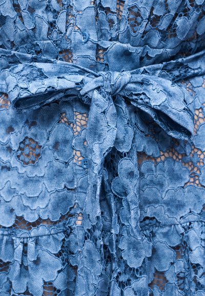 Blue lace fabric dress with floral patterns, featuring a tied bow at the waist and small blue buttons on the bodice.