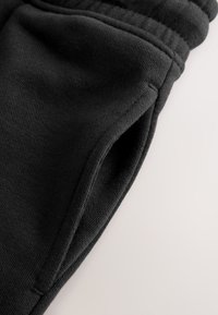 Black athletic joggers made of textured fabric, featuring a side pocket and an elastic waistband for comfort and ease of wear.