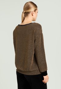 Pull marron texturé avec une coupe ample, doté d'un col noir et de manches longues. Le tissu présente un léger éclat métallique.