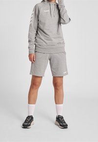 Sweat-shirt gris à capuche et manches longues, assorti à un short. Comprend un logo blanc et des accents de motif. Porté avec des chaussures de sport noires.