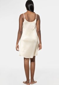 Crème-kleurige satijnen nachtjapon met verstelbare spaghettibandjes, zachte textuur en een uitlopende zoom. Gezien van achteren, met een soepele silhouet.