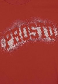 Czerwona bawełniana koszulka z krótkim rękawem, na której widnieje słowo "PROSTO" w wyraźnym, białym, postarzanym foncie, z nieregularną teksturą wokół napisu.