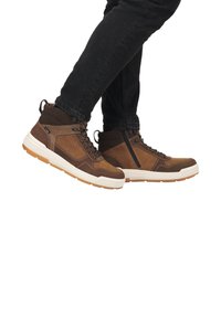 Bottines hautes marron en cuir et tissu, avec un col rembourré, des lacets robustes et une semelle crème contrastante. Elles présentent une fermeture éclair sur le côté.