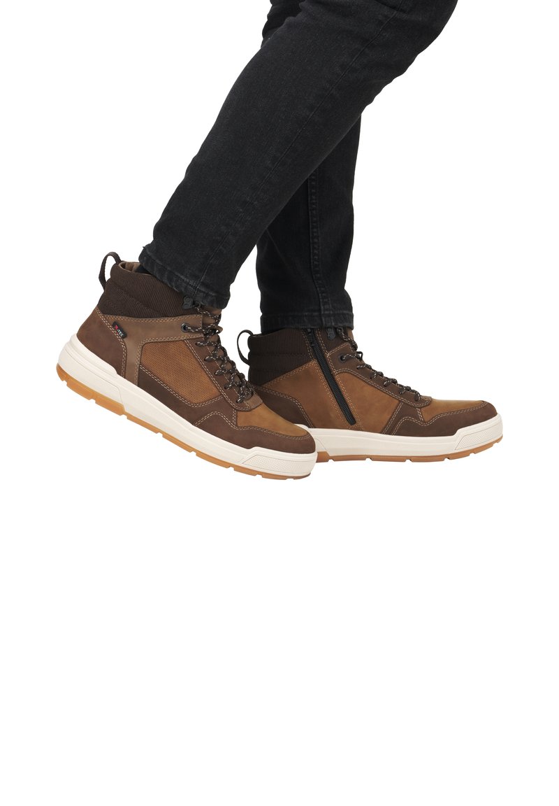 Bottines hautes marron en cuir et tissu, avec un col rembourré, des lacets robustes et une semelle crème contrastante. Elles présentent une fermeture éclair sur le côté.