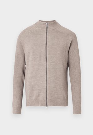 Beżowy kardigan zapinany na zamek z wysokim kołnierzem, prążkowaną fakturą na rękawach i gładkim przodem. Posiada zamek błyskawiczny z przodu. Materiał wydaje się miękki.