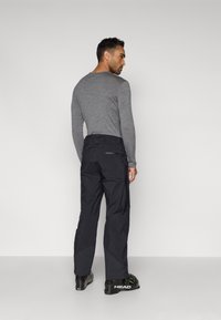 Μαύρο παντελόνι cargo με πολλαπλές τσέπες, σε συνδυασμό με γκρι μακρυμάνικο πουκάμισο. Το παντελόνι έχει άνετη γραμμή και ανθεκτική υφή.