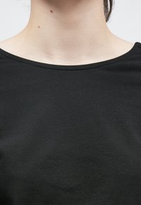 Μαύρο, κοντομάνικο τοπ από βαμβάκι, με στρογγυλή λαιμόκοψη και λείο ύφασμα. Μινιμαλιστικός σχεδιασμός χωρίς σχέδια ή διακοσμητικά στοιχεία.