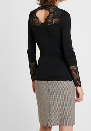 Sort langærmet top med blonderudskæring på øvre ryg og blondeærmer, båret med et knælængde hundetandsmønster-nederdel med slids bagpå.