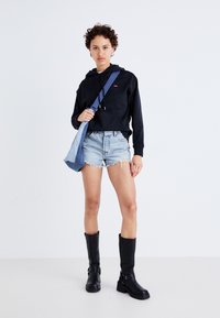 Čierna skrátená mikina, svetlé denimbové šortky a čierne čižmy po kolená. Oblečenie obsahuje modrú tašku na rameno a uvoľnený strih. Hladké textúry.