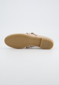 Béžová sandál s plochou gumovou podrážkou, která má dva úzké pásky a malé kovové akcenty. Logo viditelné na podrážce. Hladký povrch.