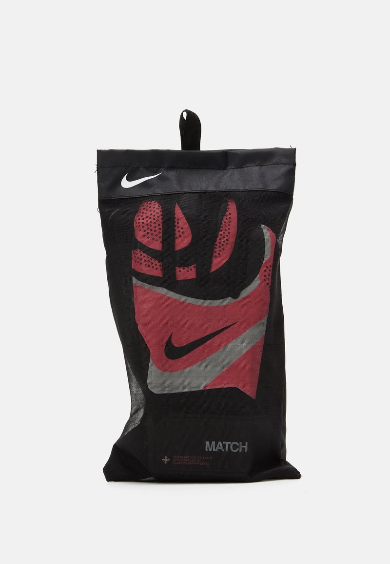 Rękawice bramkarskie Nike w czarnym opakowaniu z siateczki, z czerwonymi akcentami, wyraźnym czarnym logo oraz szarym wzorem w paski. Zawierają etykietę "MATCH".