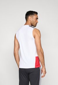 Top sport alb fără mâneci cu panou lateral roșu și dungi negre pe umeri, realizat dintr-un material neted și ușor, ideal pentru activități sportive.