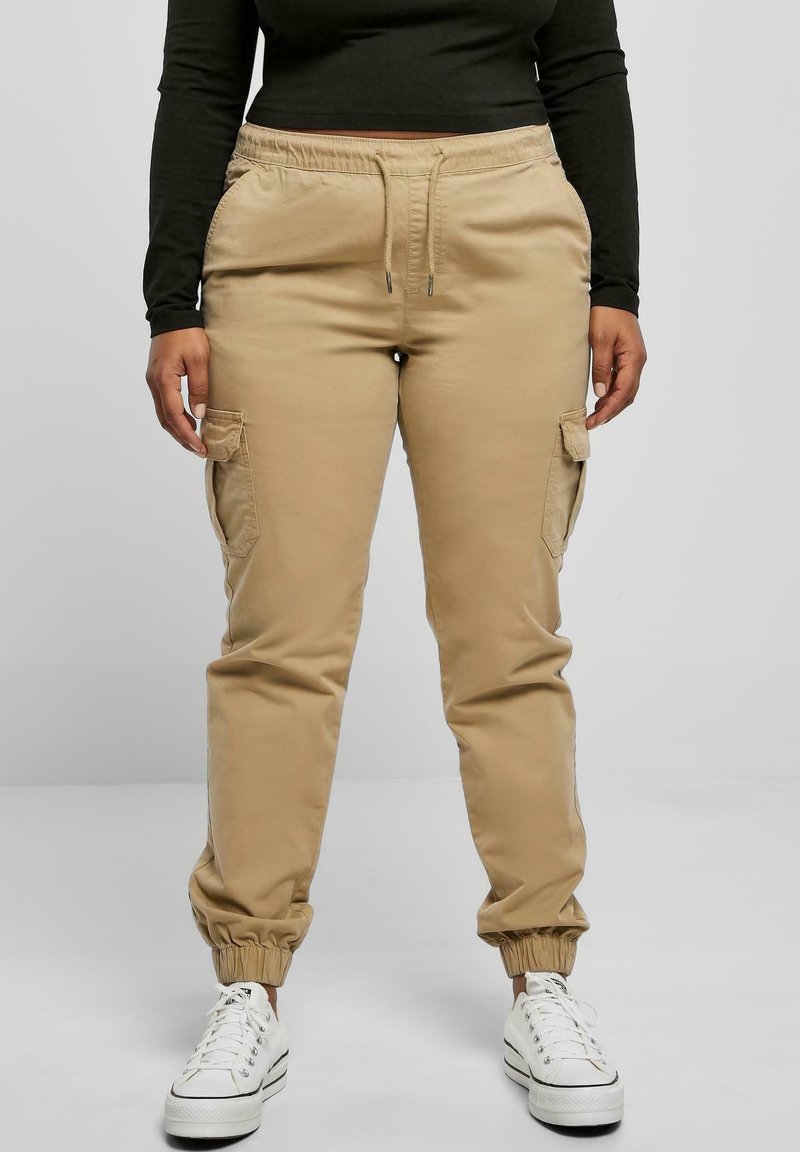 Pantalon cargo beige avec poignets resserrés, taille élastique avec cordon de serrage et poches latérales. Fabriqué en tissu doux et résistant.