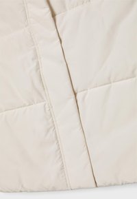 Puffjacka i ljusbeige, med quiltat mönster, slät textur och dold dragkedjestängning. Mjuk, varm material som är lämplig för kallt väder.