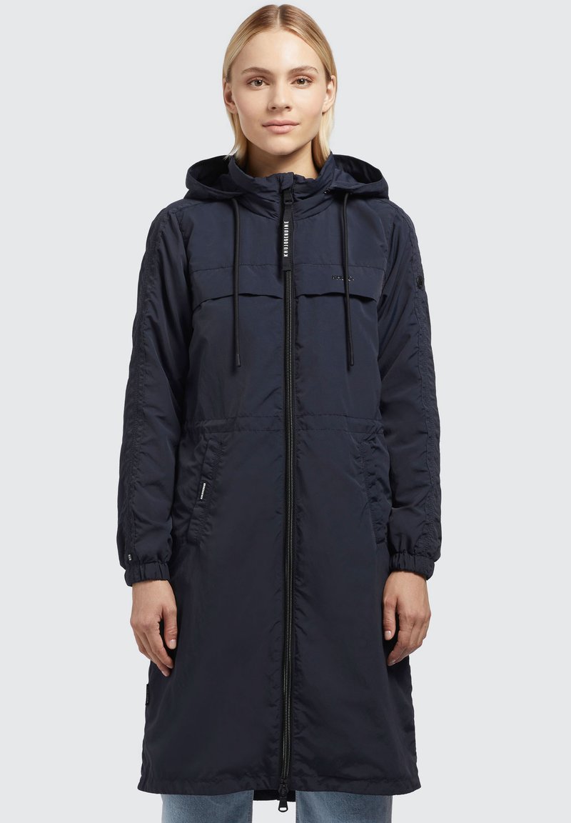 Cappotto lungo puffer blu navy con chiusura a zip, cappuccio regolabile, due tasche frontali e polsini elastici, realizzato in un tessuto liscio e leggero.