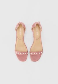 Rosa semskede hælede sandaler med en bred rem dekoreret med falske perler. Åben tå design med en ankelrem og spænde. Glat inderside.