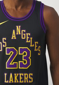Persona de piel oscura vistiendo una camiseta de baloncesto negra de los Los Angeles Lakers con el número 23 en acentos púrpura y amarillo.