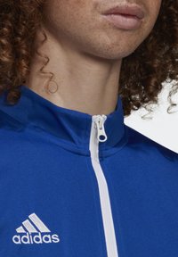 Blå sportig zip-up jacka med hög krage, i vitt blixtlås och Adidas-logotyp i vitt, slät textur och figurnära design.