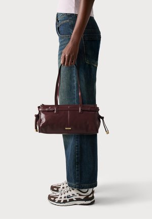 Bordeaux leren handtas met twee banden, met een slim ontwerp en subtiele hardware-accenten. Gecombineerd met losse denim jeans en sneakers.