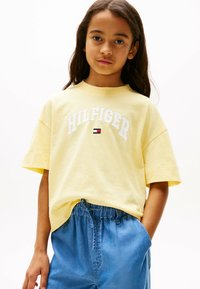 Żółta bawełniana koszulka z napisem "HILFIGER" w białym kolorze oraz małym logo. W zestawie z jasnoniebieskimi szortami dżinsowymi z elastycznym pasem.