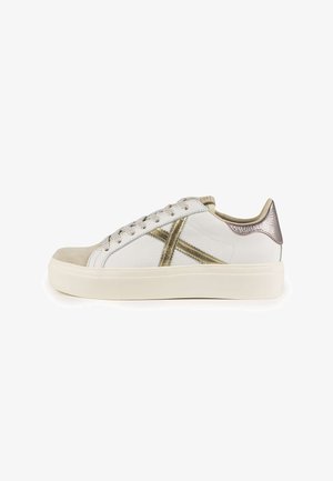 Sneaker bianco con punta in suede, dettagli metallici dorati, finitura testurizzata e un tab sul tallone lucido a contrasto.