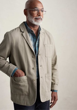Helle graue Leinenjacke mit Reverskragen, Knopfverschluss und zwei vorderen Taschen. Trägt man über einem blauen karierten Hemd mit langen Ärmeln.