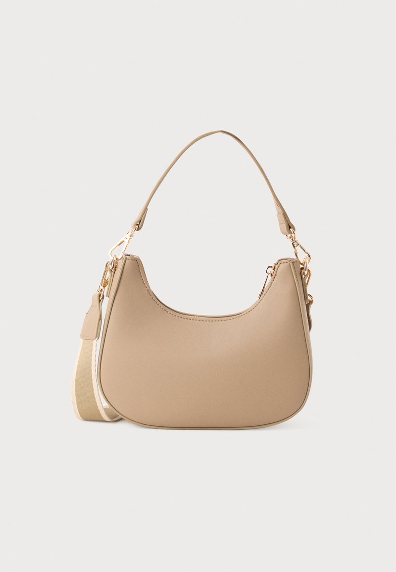 Petit sac à bandoulière beige avec un dessus arrondi, une longue bandoulière amovible et des fermoirs dorés sur fond blanc uni.