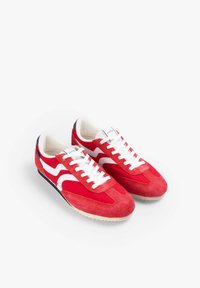 Zapatillas deportivas de ante rojo con acentos y cordones blancos, punta redonda y superficies texturizadas. Suela de goma con un diseño clásico.