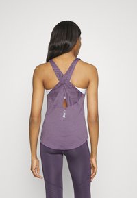 Violetti urheilullinen tank top, jossa on ristikkäiset hihnat, teksturoitu kangas ja aukko selkäpuolella. Contains kolme vaakasuoraa raitaa aukon yläpuolella.