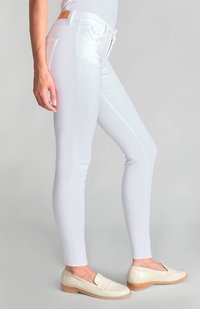 Jeans blancos ajustados hechos de una tela elástica con costuras laterales, combinados con mocasines de color claro con superficie texturizada y tacones de madera.