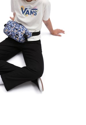 Blå blomsterbæltepose med sorte stropper, der har en lynlåslukning og logo-detalje. Båret over en hvid skjorte og sorte bukser.