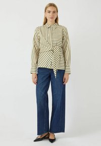 Gestreepte blouse in beige en olijf met lange mouwen en een strik taille, gecombineerd met brede donker denim jeans en zwarte puntige hakken.