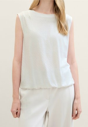 Vaaleanharmaa hihaton paita, jossa on rento istuvuus. Paidassa on hienovaraisia laskoksia olkapäillä ja pehmeä, teksturoitu kangas. Yhdistetty vaaleisiin housuihin.