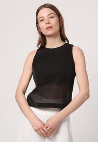Top negro sin mangas con una superposición transparente, escote redondo y un diseño corto. La tela parece suave con un brillo sutil.