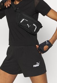 Czarna saszetka na pasku z zamkiem błyskawicznym, regulowanym paskiem i białym logo Pumy. Czarne szorty i krótki top, połączone z rękawiczkami bezpalcowymi.