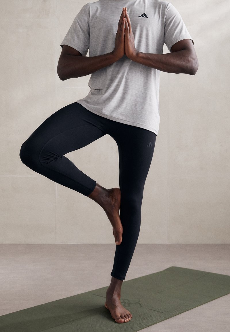 Leggings neri con un design aderente e tessuto texture, abbinati a una maglietta grigia a maniche corte con un logo. Il modello è in una posa yoga.