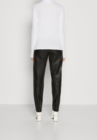 Weißes Langarmoberteil kombiniert mit schwarzen Lederhosen. Das Outfit zeichnet sich durch eine glatte Textur und eine taillierte Silhouette aus, abgerundet mit weißen Blockabsatzschuhen.