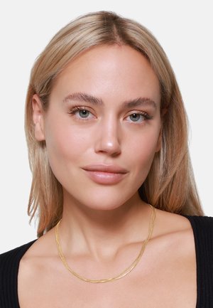 Collier en or superposé avec un design torsadé, comprenant des brins lisses et texturés. Porter sur un modèle avec des cheveux blonds de longueur moyenne.