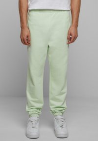 Pantalones de chándal verdes claros, confeccionados en material suave, con puños elásticos y cinturilla elástica. Llevados con zapatillas blancas.