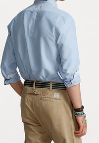 Ljusblå skjorta med uppvikta ärmar, i kombination med kaki-byxor och ett multikolor randigt bälte. Detaljer inkluderar en lapp på byxorna.