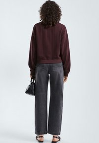 Pullover in magenta a maglia con motivo testurizzato, abbinato a jeans neri a gamba larga a vita alta. La modella tiene una piccola borsa nera.