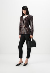 Burgundy leather jacket with gold zippers, belted waist, black fitted pants, and black handbag featuring studded accents and logo.